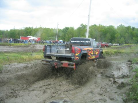 1978 Ford Bronco - A modified pickup truck navigates a muddy track with spectators in the background.
