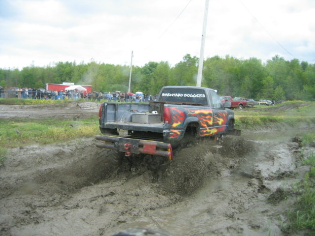 Pickup truck with flame decals driving through mud, rear view. Mud splashes up from tires