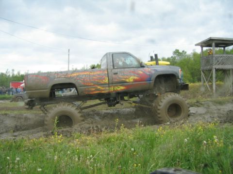 1978 Ford Bronco - A heavily modified pickup truck with large tires and flame graphics navigates a muddy track, with another vehicle visible in the background.