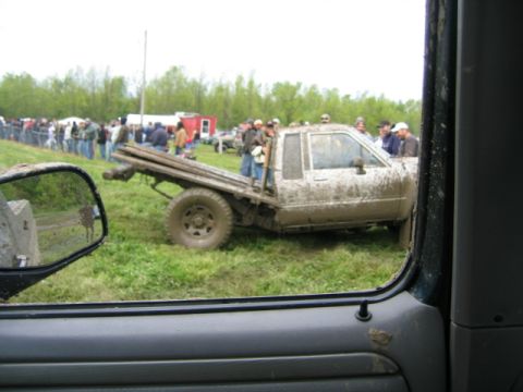 1978 Ford Bronco - A mud-covered flatbed truck appears stuck in a grassy field, with spectators gathered in the background.