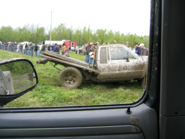 Mud-covered flatbed truck stuck in grass, viewed from inside another vehicle
