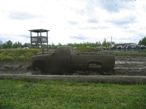 1978 Ford Bronco - A pickup truck is stuck in a mud pit, with a wooden tower and other vehicles visible in the distance.