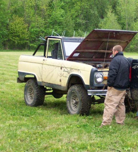 1978 Ford Bronco - A man inspects the engine bay of a vintage Ford Bronco parked in a grassy field.