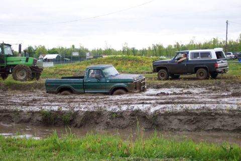1978 Ford Bronco - A green Ford pickup truck is stuck in the mud, with a dark SUV and a tractor nearby.
