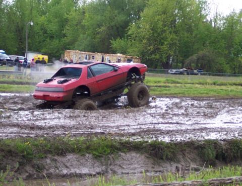 1978 Ford Bronco - A modified red Pontiac Fiero is stuck deep in a mud pit during an off-road event.