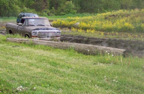 1978 Ford Bronco - A muddy 1979 Ford F-Series pickup truck navigates a rough off-road course, with another vehicle visible behind it.
