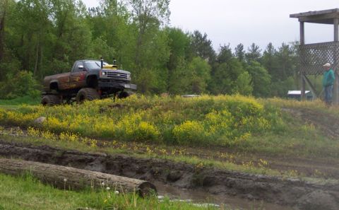 1978 Ford Bronco - A heavily modified pickup truck is positioned on a grassy hill overlooking a muddy obstacle course.