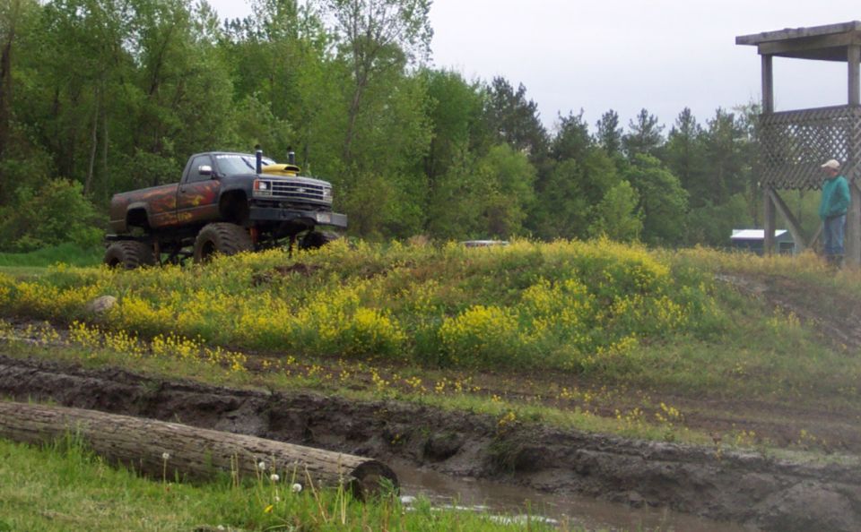 Lifted pickup truck with large tires on a muddy track, yellow flowers in foreground