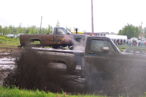 1978 Ford Bronco - Two trucks participate in a mud bogging event, with one truck creating a large splash of mud.