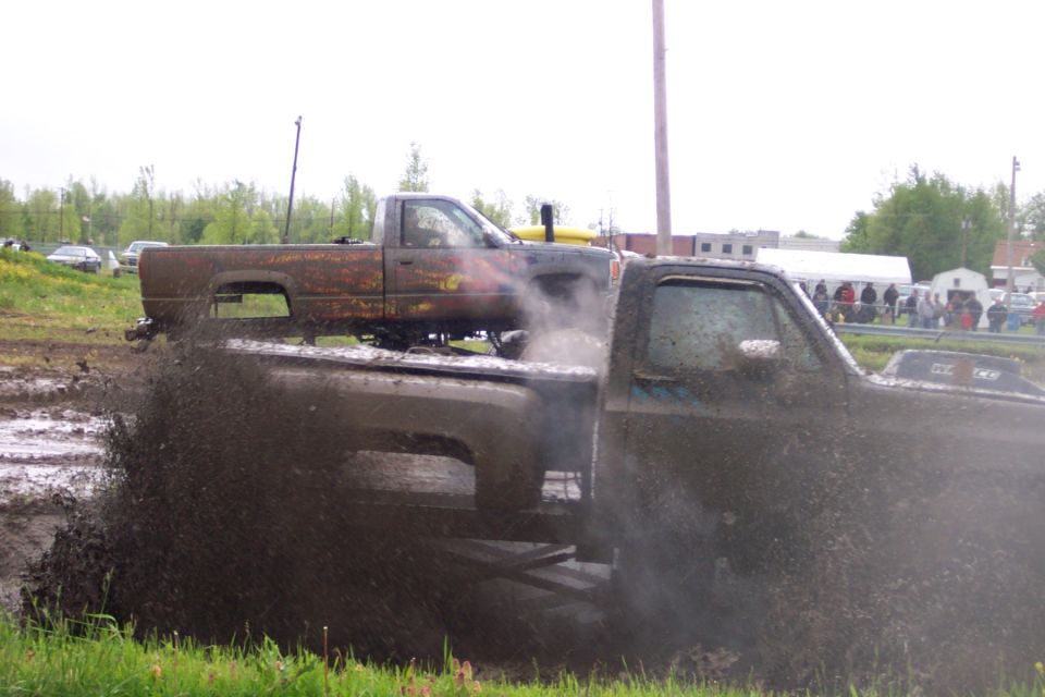 Mud bogging trucks, one splashing mud, another truck on top