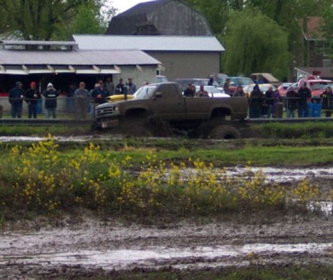1978 Ford Bronco - A pickup truck navigates a muddy obstacle course with spectators watching from a building.