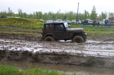 1978 Ford Bronco - A Jeep CJ-5 navigates a challenging mud pit, with other vehicles visible in the background.