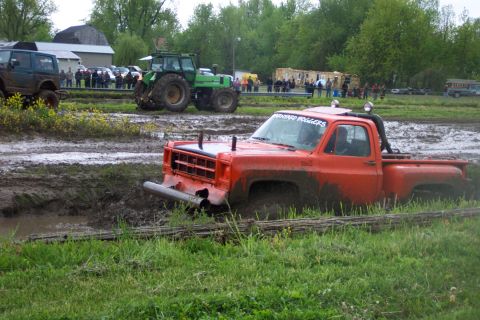 1978 Ford Bronco - An orange pickup truck is stuck in a muddy field with a tractor and other vehicles nearby.