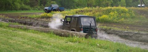 1978 Ford Bronco - Two off-road vehicles navigate a muddy track, kicking up water and dirt.