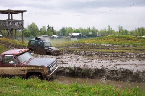 1978 Ford Bronco - Two off-road vehicles are stuck in deep mud during an event, with a wooden observation tower in the background.