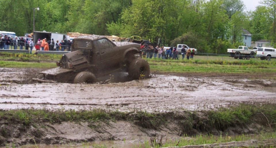 Muddy truck stuck in a mud pit with people watching in the background