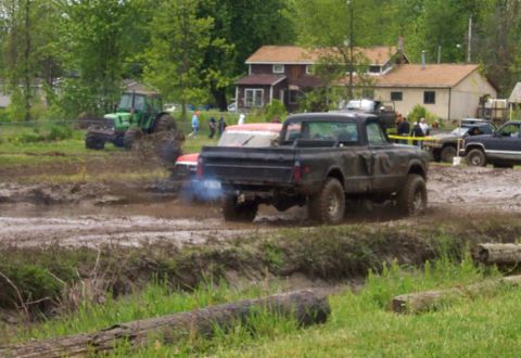 1978 Ford Bronco - Multiple vehicles, including a tractor and pickup trucks, navigate a muddy track during an event.