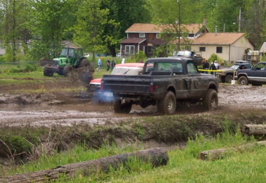 Black pickup truck with blue exhaust in mud, rear view
