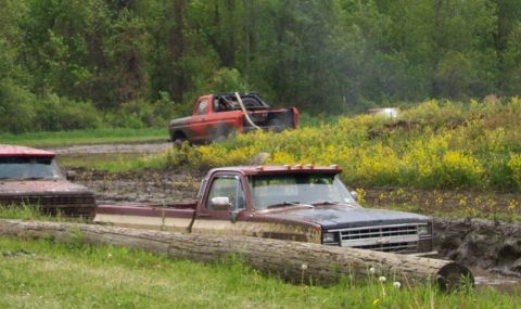 1978 Ford Bronco - Two pickup trucks are stuck in a muddy field, with one partially submerged in mud and logs.