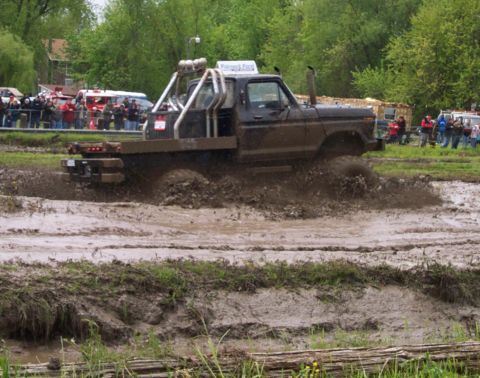 1978 Ford Bronco - A modified pickup truck navigates a muddy track, kicking up spray as it goes.
