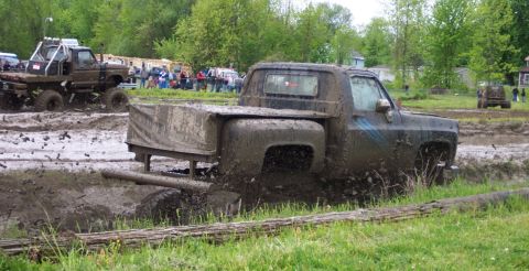 1978 Ford Bronco - A pickup truck navigates a muddy course during an event, with another vehicle visible in the background.