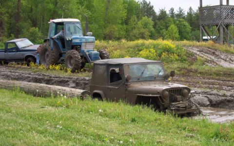 1978 Ford Bronco - A mud-covered Jeep is stuck in a muddy track, with a tractor and pickup truck nearby.