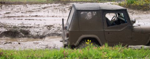 1978 Ford Bronco - A Jeep Wrangler is stuck in a muddy area with grass in the foreground.