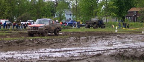 1978 Ford Bronco - A muddy pickup truck navigates a challenging mud course with spectators in the background.