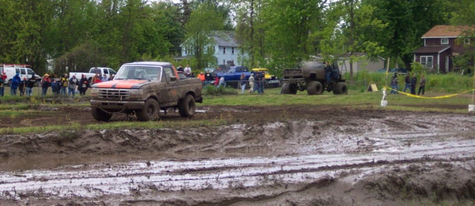 Muddy orange and brown pickup truck, 3/4 front view, 1990s model year, in a mud pit