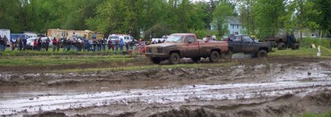 1978 Ford Bronco - Trucks navigate a challenging muddy course during an event, with onlookers watching from the sidelines.