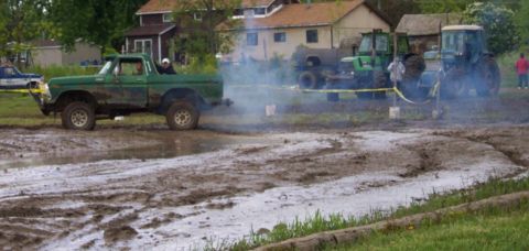 1978 Ford Bronco - A green pickup truck navigates a muddy track, with tractors visible in the background.
