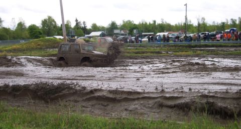 1978 Ford Bronco - Off-road vehicle navigates a challenging mud bog, kicking up a large spray.