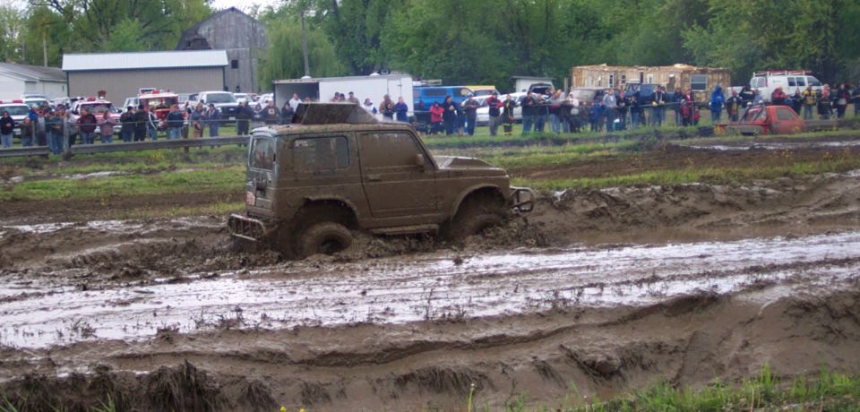 Muddy SUV stuck in a mud pit with spectators watching