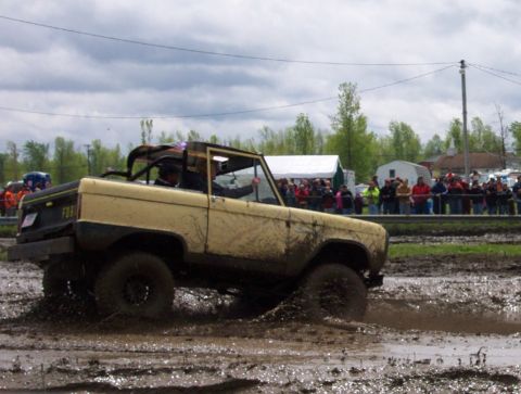 1978 Ford Bronco - A yellow 1978 Ford Bronco navigates a muddy track with spectators watching in the background.