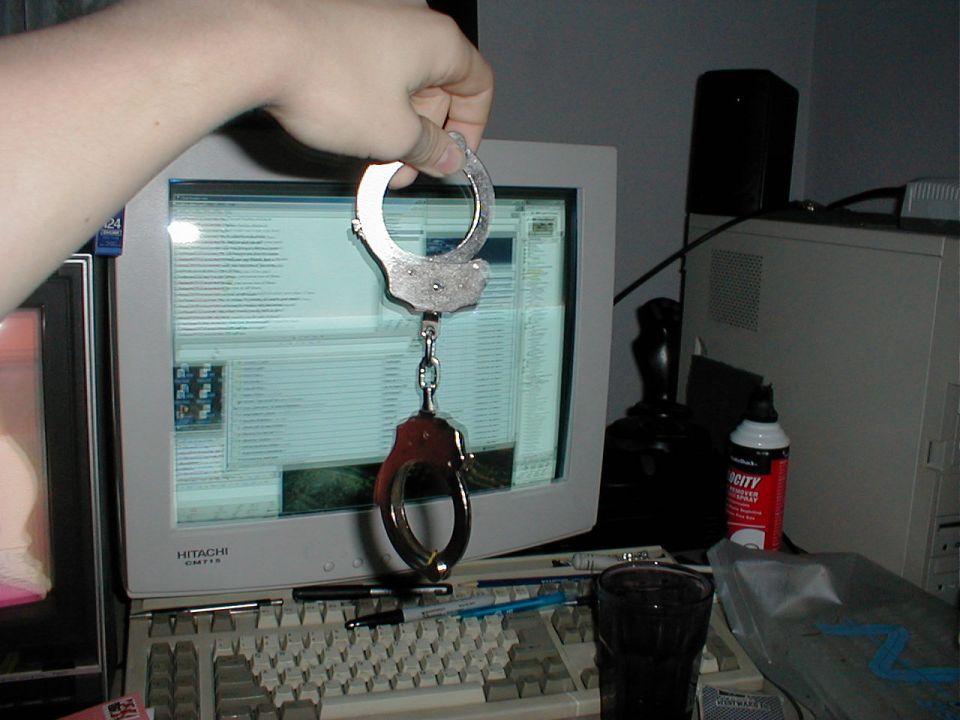 Handcuffs held over a computer monitor displaying text
