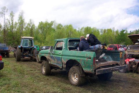 1978 Ford Bronco - Muddy 1978 Ford Bronco with passengers in the rear, seen at an outdoor event with other vehicles present.