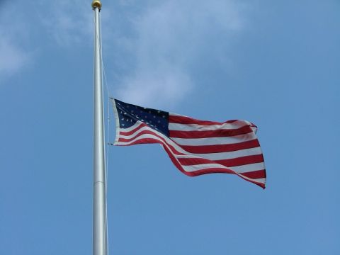 1996 Ford Probe - An American flag waves on a flagpole under a clear blue sky. The Supermotors.net logo is visible in the lower right corner.