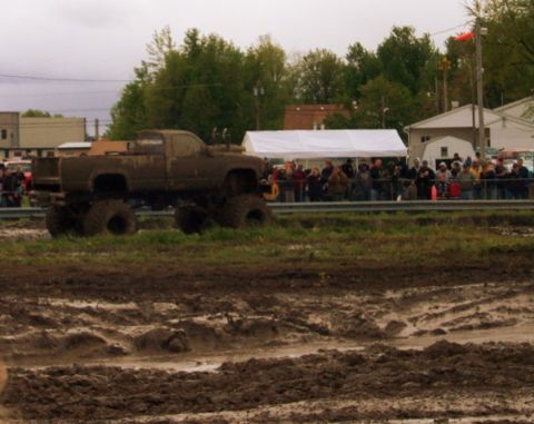1978 Ford Bronco - A heavily mud-covered monster truck navigates a muddy track in front of a crowd.