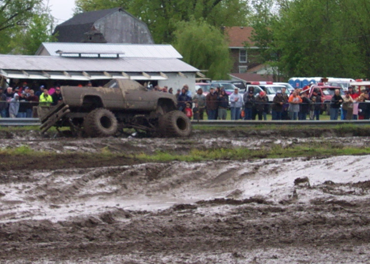 Monster truck with large tires stuck in mud, crowd watching in background