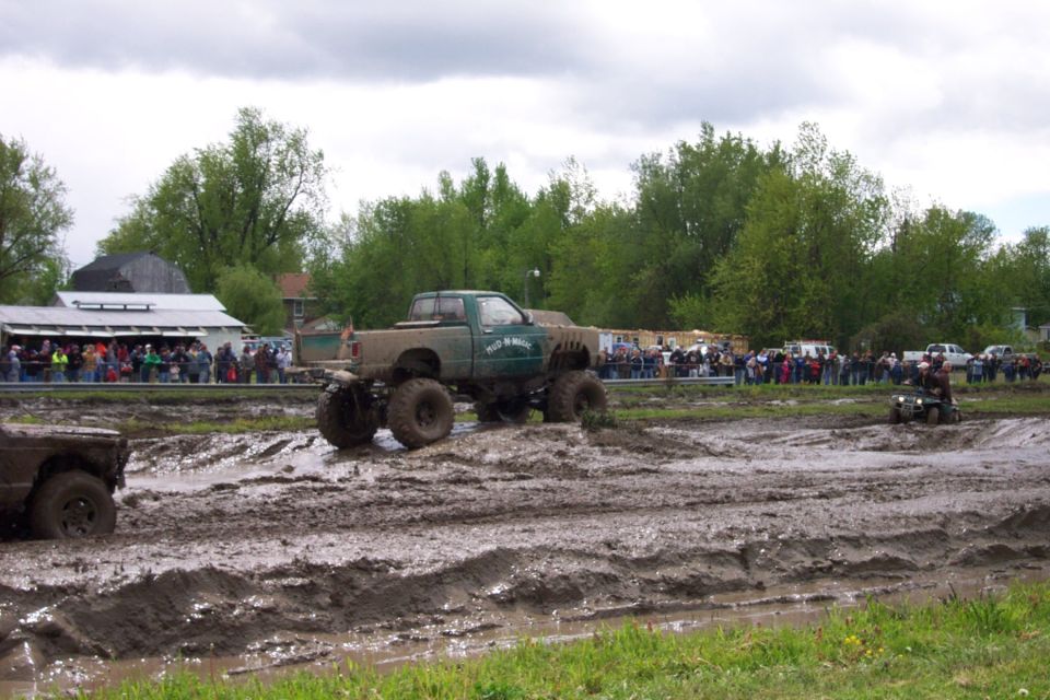 mud bogging trucks with big tires in a muddy field, crowd watching