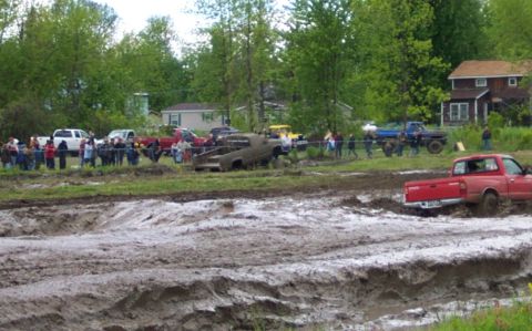 1978 Ford Bronco - Multiple trucks navigate a muddy obstacle course with spectators watching from the side.