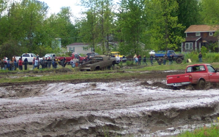 Muddy field with red Toyota Tacoma stuck in mud and other trucks in background