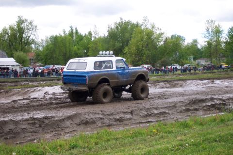 1978 Ford Bronco - A lifted, two-tone SUV navigates a muddy track with spectators in the background.