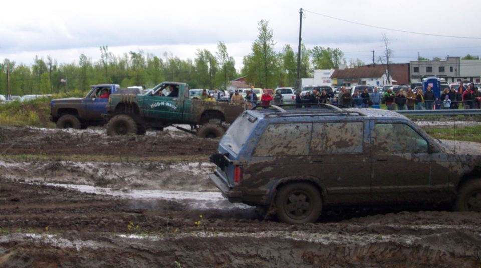 Muddy SUVs and trucks competing in a race, with spectators in the background