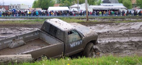 1978 Ford Bronco - A pickup truck is stuck in a mud pit during an event, with spectators watching in the background.