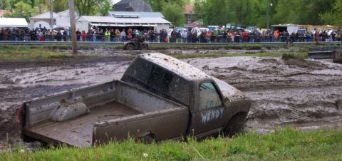 1978 Ford Bronco - A pickup truck is stuck in a mud pit during an event, with spectators watching in the background.