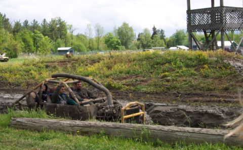1978 Ford Bronco - Four people are stuck in a muddy off-road buggy in a mud pit with a wooden structure in the background.