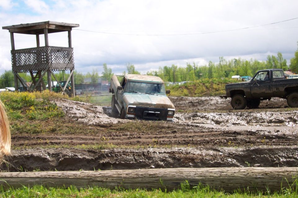 Light blue pickup truck stuck in mud pit with another truck nearby