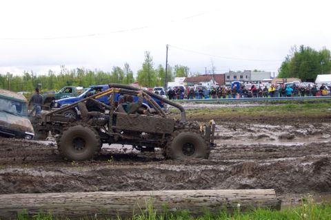1978 Ford Bronco - A heavily modified off-road vehicle navigates a muddy track during an event, with a crowd watching from the sidelines.