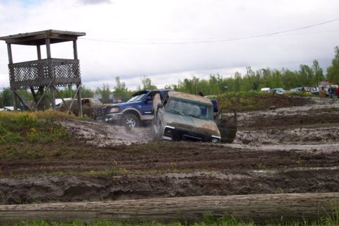 1978 Ford Bronco - Two off-road vehicles are stuck in a muddy track, with a wooden observation tower in the background.